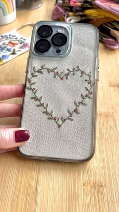 a woman's hand holding an iphone case with embroidered hearts on it