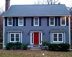 a gray house with red door and black shutters on the front porch is shown