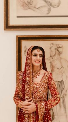 a woman in a red and gold bridal outfit standing next to two framed pictures