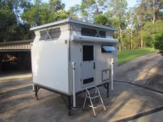 a white portable toilet sitting in the middle of a driveway next to a tree line