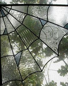 a close up of a stained glass window with trees in the background and leaves on it