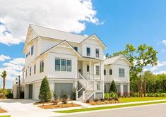 a white two story house on the corner of a street with trees and shrubs around it