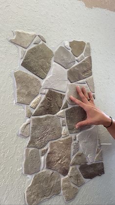 a person reaching for a piece of art made out of rocks on the wall with their hand