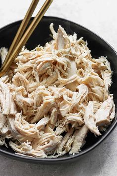 a black bowl filled with shredded chicken and two chopsticks next to each other