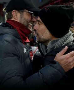 two men are embracing each other at a soccer game in winter clothes and beanies