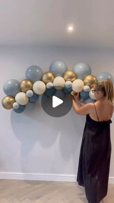 a woman in a black dress is holding balloons and placing them on the wall behind her