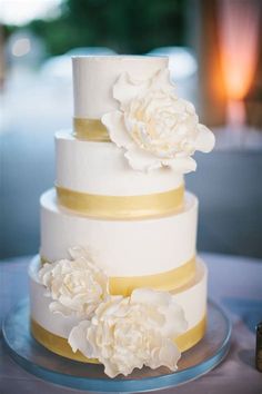 a three tiered cake with white flowers on top and gold ribbon around the edges