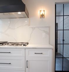 a kitchen with white cabinets and marble backsplash, along with a black range hood