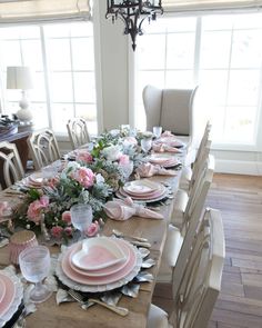 a dining room table set with pink and white plates, napkins and flowers on it