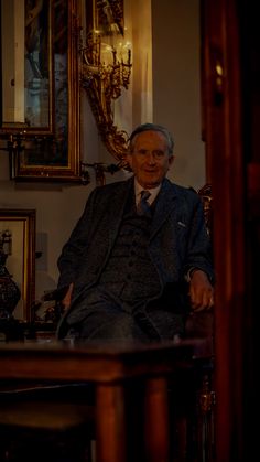 an old man sitting in a chair next to a table with pictures on the wall