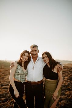 two women and an older man posing for a photo in the middle of a field