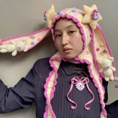 a woman wearing a crocheted hat with flowers on it's head and holding her hands in the air