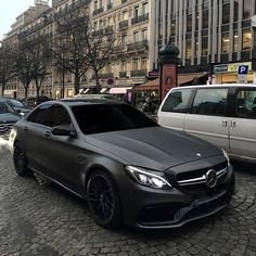 a black mercedes parked on the side of a street next to other cars and buildings