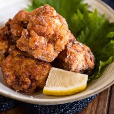 some fried food on a white plate with lemon wedges