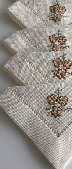 three embroidered napkins with flowers on them sitting on a white tablecloth covered surface