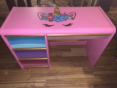 a pink desk with an unicorn face painted on the top and drawers underneath it,