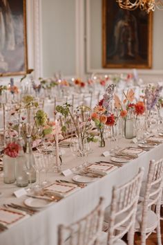 a long table with many vases filled with flowers and place settings on top of it