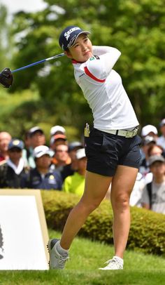 a woman swinging a golf club on top of a lush green field next to a crowd