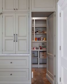 an open pantry with white cabinets and drawers in the middle of a wood floored room