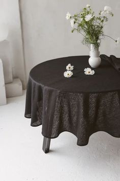 a black table cloth with white flowers in a vase on it and an empty chair