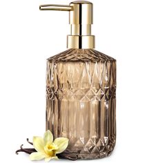 a glass soap dispenser with a flower on the side and a gold faucet next to it