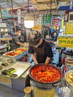 a man standing in front of a large pot filled with food on top of a table