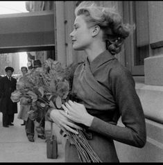 a woman is walking down the street with flowers in her hand and people behind her