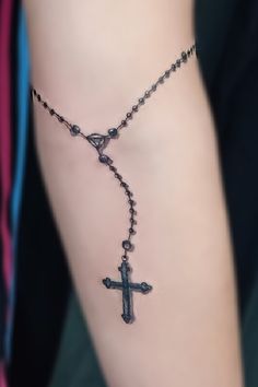 a woman's arm with a rosary and cross tattoo on the side of it