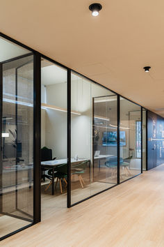 an office with glass walls and wooden flooring is seen from the hallway to the dining room