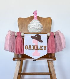 a pink and brown 1st birthday banner with a cupcake in the middle on a wooden chair