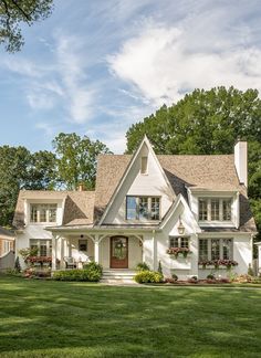 a large white house with lots of windows and plants on the front lawn, surrounded by lush green grass