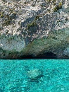 the water is crystal blue and there are rocks on the side of the cliff in the background