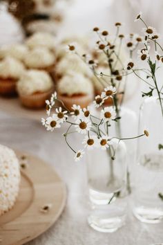 small vases filled with white flowers on a table next to muffins and cupcakes