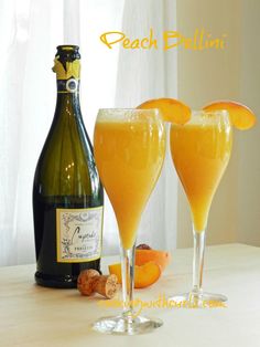 two champagne glasses filled with orange juice next to a bottle