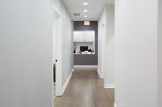 an empty hallway with white walls and wood flooring, leading to a computer desk