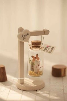 a small glass jar filled with sand sitting on top of a white tile floor next to wooden