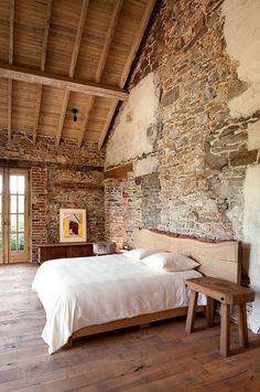 a bed sitting in a bedroom next to a stone wall and wooden floored walls