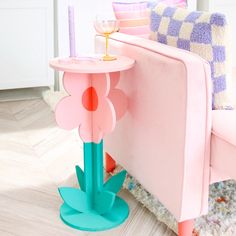 a pink chair with a candle on it next to a flower shaped side table in front of a couch