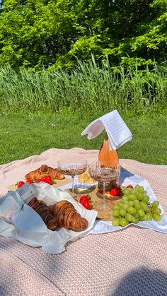 a table with bread, grapes and wine on it in the grass next to some trees