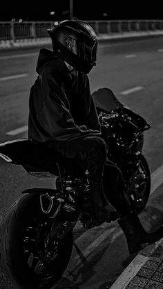 black and white photograph of a person on a motor bike wearing a helmet sitting in the street