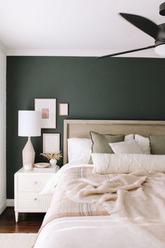 a bedroom with green walls, white bedding and a ceiling fan in the corner