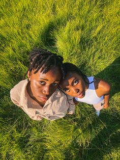 two young women laying in the grass looking up at the camera with their heads together