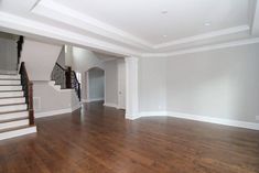 an empty living room with hard wood flooring and white paint on the walls, along with stairs