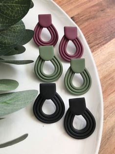 three pairs of earrings sitting on top of a white plate next to green plants and leaves