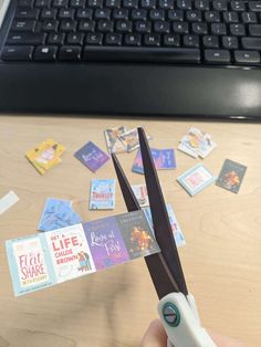 someone is holding scissors with some stickers on the table next to their computer keyboard