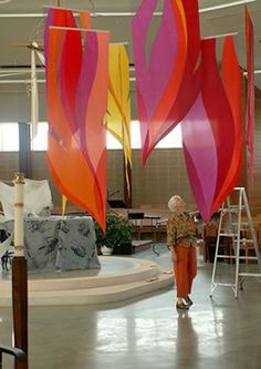 a woman is standing in front of some large colorful flags hanging from the ceiling,