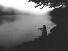 a person standing next to a body of water on a foggy day with a light in their hand