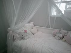 there is a bed with white curtains and stuffed animals on the bottom half of it