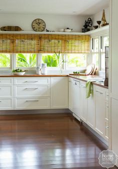 a large kitchen with white cabinets and wooden floors is pictured in this image, there are two clocks on the wall above the counter