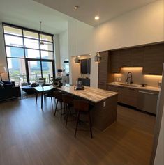 an open kitchen and living room area with hardwood floors, large windows, and modern furnishings